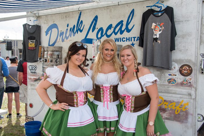 One brunette woman and two blonde women pose wearing dirndls, posing in front of the Drink Local beer truck.