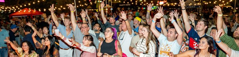 The crowd stands with their hands in the air looking at the stage. People are excited and smiling.