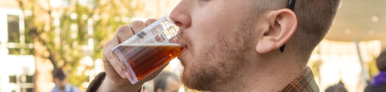 Close up of a man sipping a beer from a tasting glass.