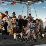 Group of brass musicians in traditional German clothing play on stage.
