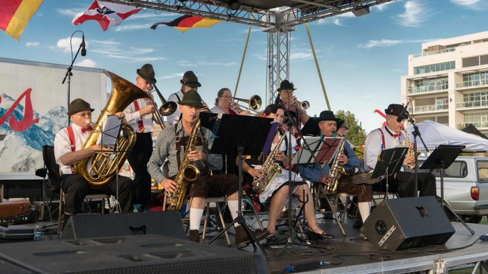 Group of brass musicians in traditional German clothing play on stage.