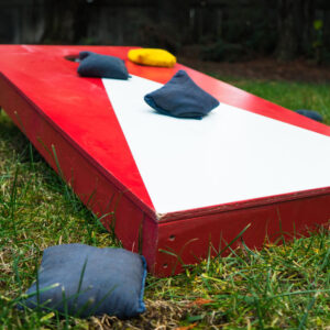 Red and white cornhole board with blue and yellow bags.