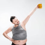 Man with shirt pluued up to show belly, hoisting beer over head.